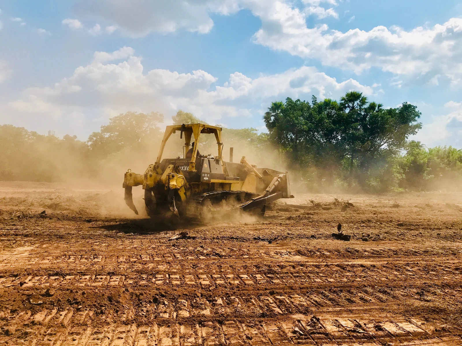 Tracked bulldozer clearing dusty ground on an open construction site.