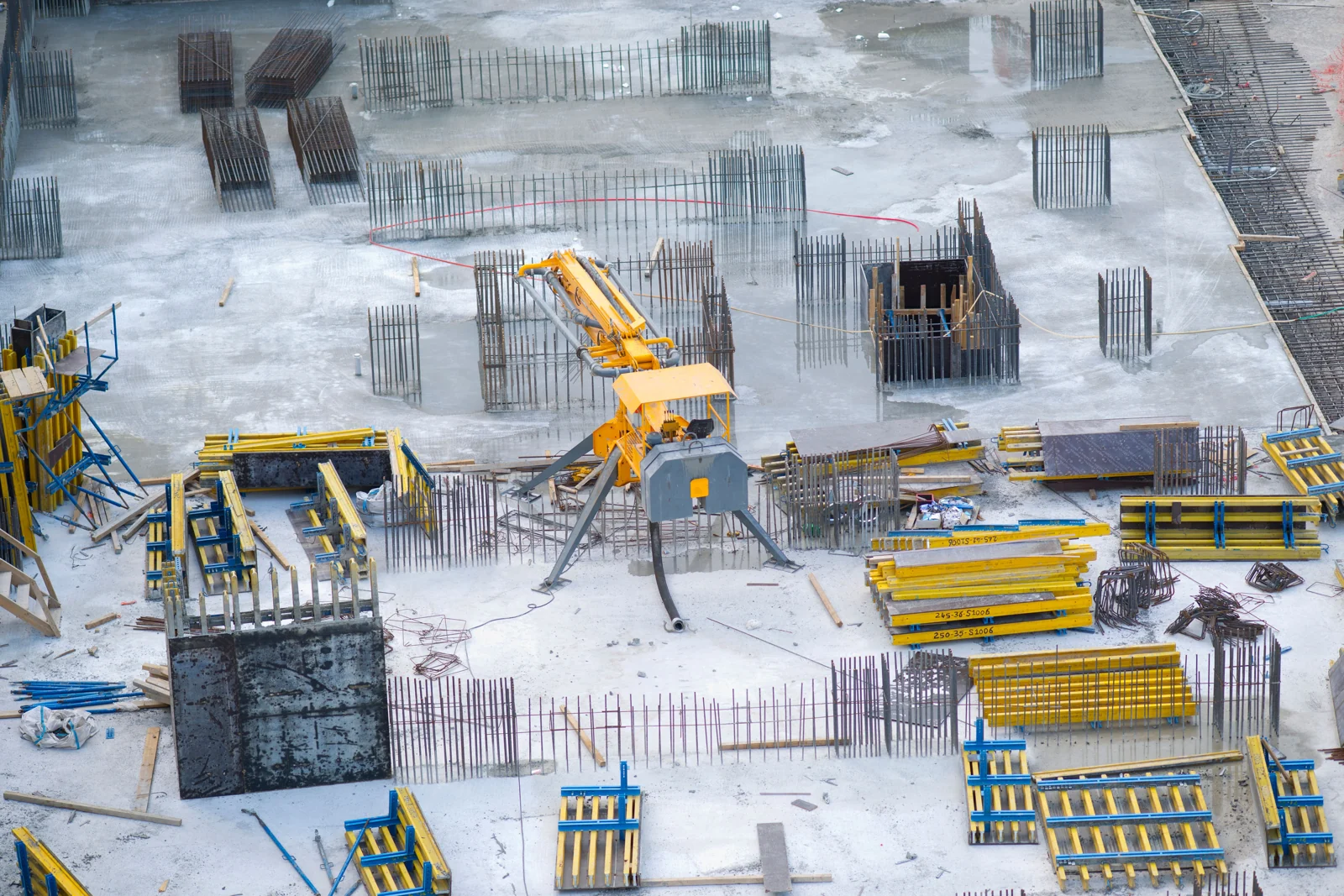 Concrete foundation slab with upright rebar, yellow formwork and site machinery.