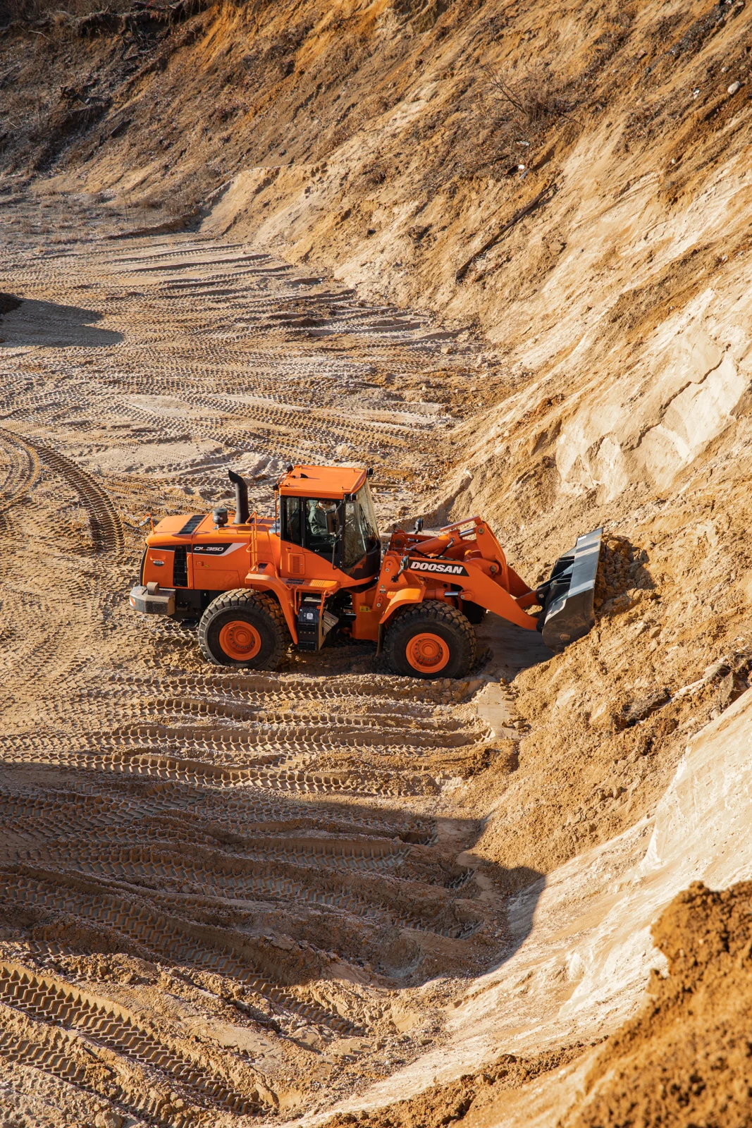 Orange wheel loader working at a sandy bank, viewed from above.